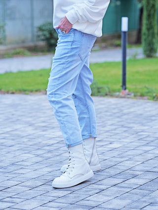 Person trägt OFF#DLY Denim Destroy Thea lightblue Jeans mit leicht umgeschlagenem Saum und markantem Schriftprint. Die Jeans hat eine entspannte Passform und wird mit weißen High-Top-Boots kombiniert.