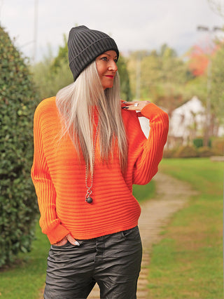 Eine Person trägt den OFF#DLY Pulli Cara orange, einen gerippten, leicht verkürzten Pullover mit lockerer Passform. Ergänzt mit einer langen Kette, vermittelt er cozy Chic.