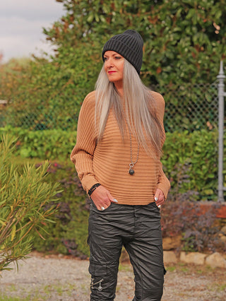 Erwachsener trägt den OFF#DLY Pulli Cara camel mit gerippter Struktur, kombiniert mit lässigen schwarzen Cargo-Hosen und dunkler Mütze, in einer entspannten Outdoor-Umgebung.