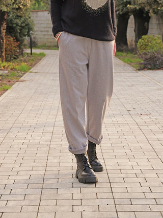 Person trägt OFF#DLY Hose Ronja grau, locker sitzende, hellgraue Hose mit umgeschlagenen Bündchen. Kombiniert mit klobigen, schwarzen Schnürstiefeln auf heller Pflastersteinterrasse, ideal für Komfort und Vielseitigkeit im Alltag.