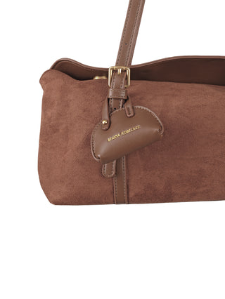 Nahaufnahme der Regina Schrecker Long Bag Velours brown, einer braunen Wildleder-Schultertasche mit goldfarbener Schnalle am Lederriemen und einem kleinen, goldgeprägten Lederanhänger mit REGINA SCHRECKER.