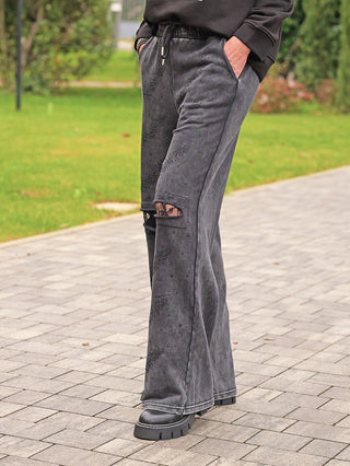 OFF#DLY Joggingpant Glitzer Destroy black: Locker sitzende, anthrazitfarbene Hose mit Destroy-Knie, die schwarze Netzstrumpfhose zeigt, Glitzerakzente, weites Bein, Kordelzugbund, kombiniert mit klobigen schwarzen Stiefeln für einen rockigen Glam-Look.