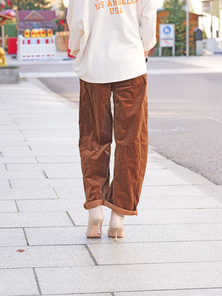 OFF#DLY Cord Pant Tabea camel: Person trägt locker geschnittene, umgeschlagene braune Cordhose, kombiniert mit nudefarbenen Pumps auf Bürgersteig. Lässiger, moderner Look mit angenehmem Tragekomfort und dezenter Vintage-Note.