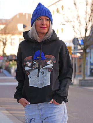 Frau trägt OFF#DLY Sweat DOG black Hoodie mit humorvollem Grafikprint: drei Hunde mit Sonnenbrillen lesen die Daily Dog. Kombiniert mit Jeans, ideal für lässigen Streetstyle.