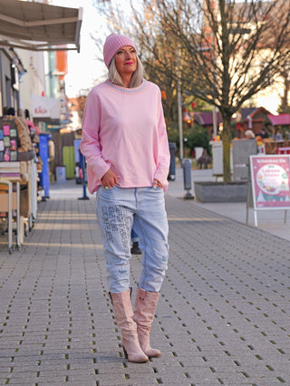 Frau trägt den OFF#DLY Sweater Lecco rose in lockerem Schnitt, kombiniert mit hellblauen Jeans. Der Pullover hat einen Rundhalsausschnitt und verleiht einen entspannten, femininen Look.