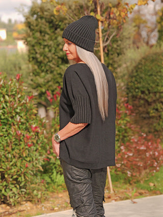 Frau trägt den OFF#DLY Pulli Angelina black, ein locker geschnittenes, kurzärmeliges, schwarzes Oberteil aus weichem Material, ergänzt durch eine goldfarbene Armbanduhr.