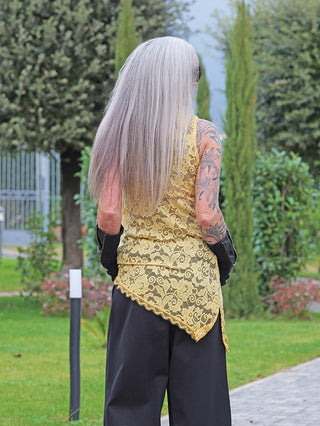 Person mit langem, silbrig-grauem Haar trägt das OFF#DLY Spitzen Top gelb – ein ärmelloses, spitzenbesetztes Oberteil mit hohem Kragen und asymmetrischem Saum, kombiniert mit schwarzen Handschuhen.