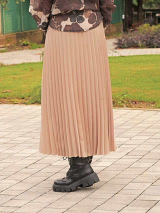 OFF#DLY Plissee Rock beige: Eleganter, beige Plisseerock in Midi-Länge, kombiniert mit schwarzen, klobigen Schnürstiefeln, sichtbar auf einem gepflasterten Weg getragen. Perfekt für vielseitige Outfits.