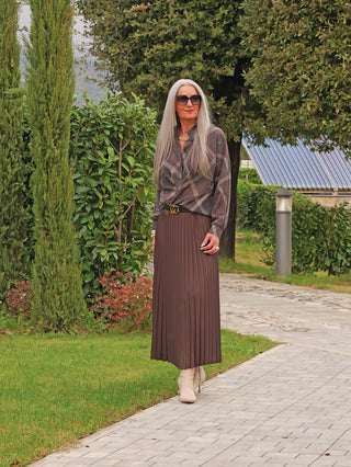 Frau im Garten trägt OFF#DLY Bluse Tanja asphalt/mix, braun gemustert, in dunklem Faltenrock. Die Bluse hat fließenden Schnitt, kombiniert mit beigen Stiefeletten und dunkler Sonnenbrille.