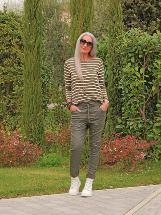 Ältere Frau trägt das OFF#DLY Ringel Donna khaki Shirt mit horizontalen Streifen, kombiniert mit olivgrünen Jogger-Hosen und weißen Sneakers, accessoriert mit Schmuck.