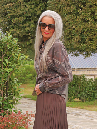 Die ältere Frau trägt die OFF#DLY Bluse Tanja asphalt/mix mit grafischem Muster, kombiniert mit einem passenden Rock. Die Bluse besticht durch ihren fließenden Schnitt und elegante Optik.