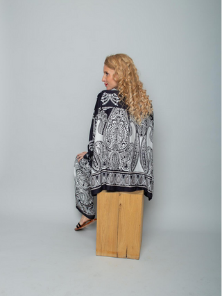 Emily Bluse 8881-157910 black/white in einem Studio von hinten aufgenommen: Lässige, schwarz-weiß gemusterte Paisley-Kimono-Bluse mit weiten Ärmeln und passender Hose, getragen von einer Person mit langen, blonden Locken.