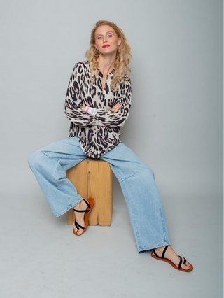 Junge Frau trägt die Emily Bluse 8812-154520 leo, eine locker sitzende, langärmelige Bluse mit Leo-Print, kombiniert mit hellen Jeans und schwarzen Sandalen, in einem entspannten und modischen Studio-Setting.