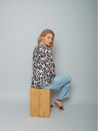 Emily Bluse 8812-154520 leo: Frau in lockerer, langärmeliger Leo-Print-Bluse aus Viskose, mit neonfarbenem Strickbund am Ärmelsaum, sitzt seitlich, blickt zurück zur Kamera.