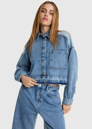 Junge Frau trägt ALIX Denim Blouse light blue Denim, eine verkürzte, oversized Jeansjacke mit Brusttasche und rohem Saum, kombiniert mit hochgeschnittenen, lockeren Jeans für einen lässigen Look.
