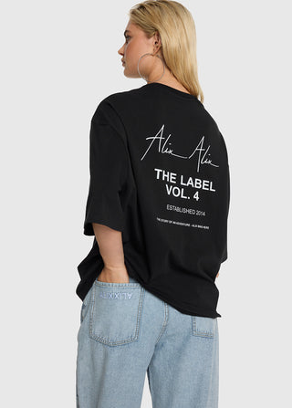 Person von hinten in einem übergroßen ALIX Bull Tee schwarz mit großem weißen Rückendruck ALIX THE LABEL VOL. 4, kombiniert mit weitem Jeans. Lässiger, moderner Look.