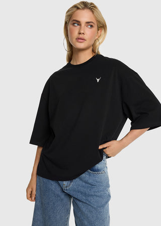 Junge Frau trägt ALIX Bull Tee black, ein oversized schwarzes T-Shirt mit kleinem Bullhead-Logo auf der Brust, kombiniert mit hoch taillierten blauen Jeans und großen Creolen.