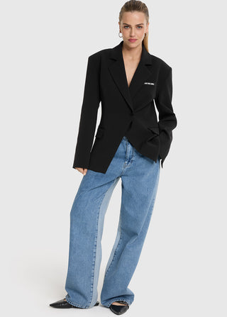 Model trägt den ALIX Fitted Blazer black mit taillierter Silhouette, Schulterpolstern und Ein-Knopf-Verschluss, kombiniert mit weiten Jeans, schwarzen Flats und goldenen Creolen.