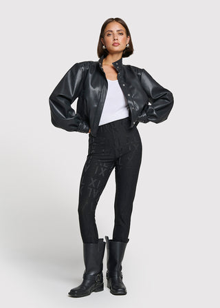 Frau trägt ALIX Jacquard Legging black, eine hochgeschnittene, eng anliegende Legging mit subtilen Logo-Prints, kombiniert mit einer schwarzen, kurzen Lederjacke und weißen Tanktop, ideal für einen urbanen Look.