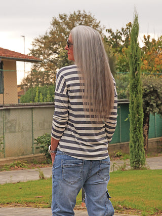 Person von hinten mit langem, silbrig-grauem Haar, trägt das OFF#DLY Ringel Glitzer Delia marine Shirt mit feinem Glanzakzent, kombiniert mit blauer Jeans und Sonnenbrille, stehend im Freien.