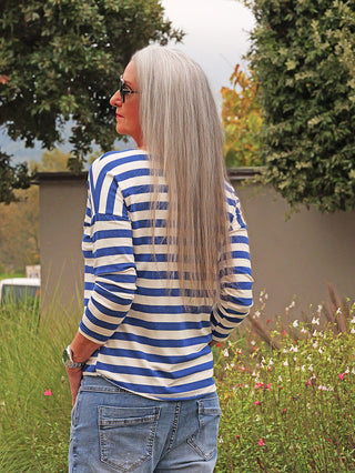 Person in einem OFF#DLY Ringel Glitzer Delia royalblue Shirt mit dezentem Glitzereffekt, trägt Jeans, Uhr und Sonnenbrille, steht mit Rücken zur Kamera, Hände in den Taschen.