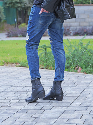 Person trägt OFF#DLY Destroy Denin Star midblue Jeans mit markanten Destroy-Details und dekorativen Patches. Sichtbar sind die Beine in schmal geschnittenen, leicht gekrempelten Jeans.