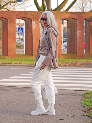 Person in urbaner Umgebung trägt OFF#DLY White Denim Mira: locker geschnittene, weiße Jeans, die an den Bündchen hochgekrempelt ist, kombiniert mit taupefarbenem Blazer und weißen Schnürstiefeln.