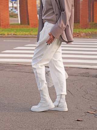 Person trägt OFF#DLY White Denim Mira, leicht konisch geschnitten, mit aufgeschlagenen Bündchen. Die Jeans kombiniert stilvoll zu weißen Stiefeln und taupefarbenem Blazer, ideal für lässige Eleganz.