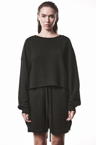 Frau trägt den Thom Krom WS496 Sweat black, einen oversized schwarzen Sweatshirt mit rohem, leicht verkürztem Saum und gerippten Abschlüssen, kombiniert mit locker sitzenden Shorts.