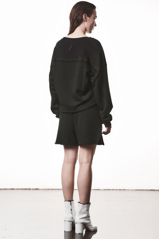 Person von hinten in Thom Krom WST 432 Hose black, einer schwarzen Shorts mit elastischem Bund und offenen Saumkanten, kombiniert mit weißem, mittelhohem Stiefel.