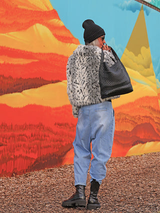 Person von hinten vor einem bunten Wandbild, trägt OFF#DLY Denim Hella lightblue, locker geschnittene, leicht zulaufende Jeans, kombiniert mit groben schwarzen Lederstiefeln und einer großen schwarzen Tasche.