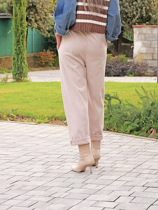 Person trägt OFF#DLY Hose Ronja beige, locker geschnitten mit umgeschlagenen Bündchen, kombiniert zu beigen Stiefeletten. Der Look wird durch einen gestreiften Pulli und Jeansjacke ergänzt.