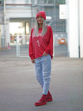 Person in urbaner Umgebung trägt OFF#DLY Destroy Denim Frieda lightblue Jeans mit dezenten Used-Details, kombiniert mit rotem Pullover und passenden Boots. Lässiger, moderner Look, perfekt für den Alltag.