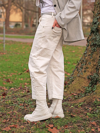 Die OFF#DLY White Denim Nina zeigt sich in einem modernen, leicht verkürzten Schnitt, kombiniert mit eleganten, passenden High-Top-Boots in einem herbstlichen Parksetting.