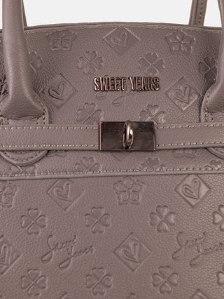 Nahaufnahme der Sweet Years Tote Bag grey, einer Henkeltasche aus taupefarbenem Kunstleder mit Klee- und Herzmotiven, verziert mit einer kleinen metallischen Markenplakette und einem horizontalen Riemen mit Metallschnalle.