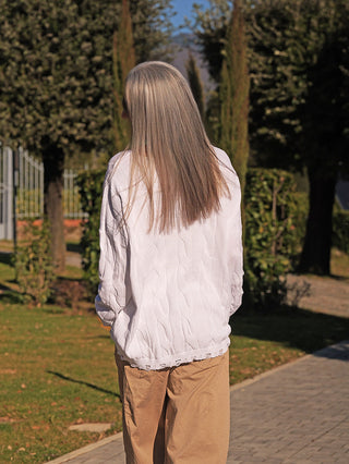 Eine Person trägt den OFF#DLY Pulli Agathe white, einen locker geschnittenen, weißen Pullover mit feinem Strukturmuster, während sie auf einem Gartenweg steht.