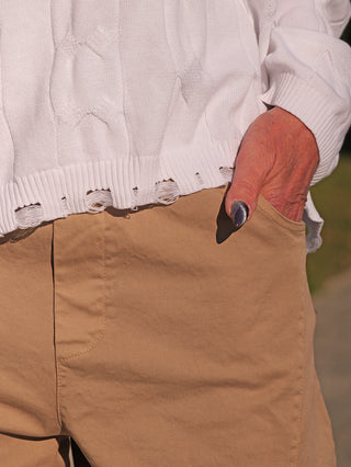 Nahaufnahme des OFF#DLY Pulli Agathe white, ein weißer Strickpullover mit leicht ausgefranstem Saum. Die rechte Hand mit grauem Nagellack steckt in der Tasche einer beigefarbenen Hose.