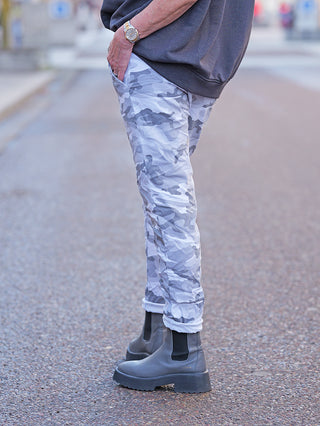 Person trägt OFF#DLY Camo Joggpant grau/weiß mit Camouflage-Muster und schmalem Bein, kombiniert mit schwarzen Chelsea-Boots. Die Hose ist lässig, komfortabel und ideal für urbane Styles.