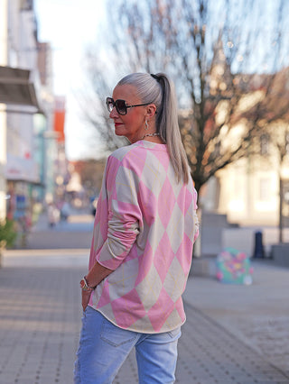 Eine silberhaarige Frau trägt das OFF#DLY LS Karo rose/taupe, ein locker sitzendes Longsleeve mit modernem Rautenmuster, kombiniert mit hellen Jeans, während sie auf einer Einkaufsstraße spaziert.