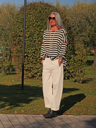 Frau in Park trägt OFF#DLY Joggpant Melania creme, locker geschnittene Hose mit Seitentaschen, kombiniert mit gestreiftem Oberteil und schwarzen Stiefeln, vermittelt lässige Eleganz.