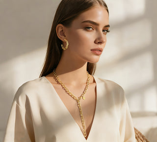 Junge Frau trägt die OFF#DLY Gliederkette Y Gold. Die vergoldete Y-förmige Kette fällt elegant ins Dekolleté, ergänzt durch passende, auffällige Ohrringe. Ihr Look ist schlicht und anspruchsvoll.