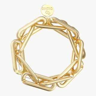 Das OFF#DLY Gliederarmband gold zeigt ein starres Armband mit übergroßen, papierclipartigen Gliedern und einem kleinen runden Anhänger mit Logo, gefertigt aus einer Zinklegierung.