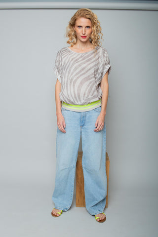 Die Emily Bluse 158240 taupe zeigt ein locker geschnittenes Blusenshirt mit Zebra-Muster und neon-gelbem Saumband, kombiniert mit weiten, hellen Jeans und gelben Sandalen.