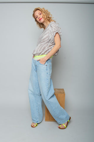 Emily Bluse 158240 taupe: Locker sitzendes, kurzärmeliges Blusenshirt mit blassem Zebra-Muster und neon-gelbem Saumband, getragen von einer Frau in weiten Jeans und passenden Sandalen.
