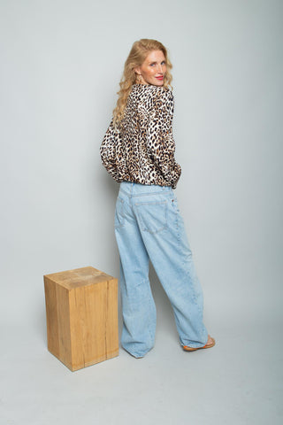 Emily Bluse 158560 Leo aus weicher Viskose, langärmelig mit lässigem Leopardenmuster, getragen von einer Frau mit weiten Jeans. Sie steht vor einem schlichten Hintergrund, leicht über die Schulter blickend.