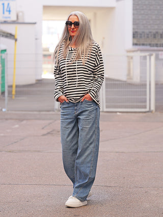 Person in True Religion Ruby Volume Denim, weite blaue Jeans mit Five-Pocket-Style und hohem Bund, kombiniert mit schwarz-weiß gestreiftem Oberteil, steht vor Gebäude mit 14 Schild.