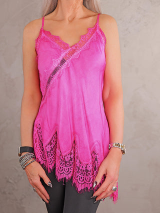 Person trägt das OFF#DLY Top Violetta pink mit edler Spitze am Dekolleté und asymmetrischem Saum, kombiniert mit dunkler Hose und silbernen Accessoires. Ideal für vielseitige, elegante Outfits.