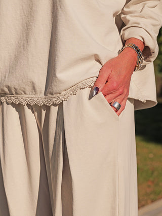 Nahaufnahme eines Arms in der Tasche einer locker geschnittenen, hellbeigen Hose, getragen mit dem OFF#DLY Longsleeve Liv eisgrau, verziert mit zarter Spitze am Saum.