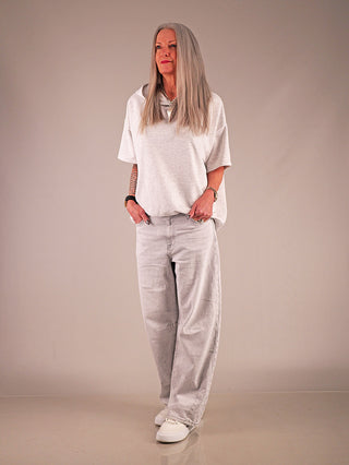 Frau trägt OFF#DLY Wide Leg Denim Greta lightgrey, mit weitem Barrel Fit und entspannter Silhouette, kombiniert mit lässigem Oberteil und Sneakers, vermittelt minimalistischen, urbanen Stil.