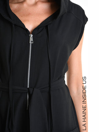 La Haine Jumpsuit M5348 black: Nahaufnahme eines ärmellosen, schwarzen Jumpsuits mit Kapuze, vorderem Reißverschluss, Taillenbindegürtel, Kordelzug an der Kapuze, und vertikalem Schriftzug “LA HAINE INSIDE US”.